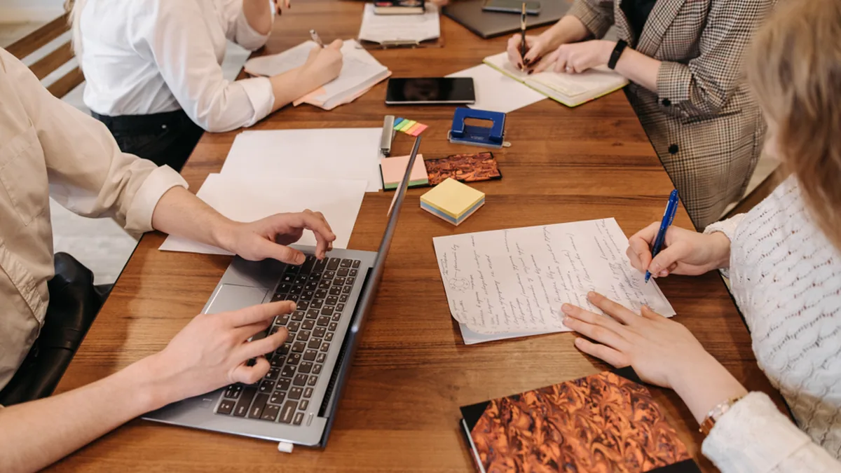 Adults collaborating around a table with a laptop, notes and notebooks during a project-planning session.
