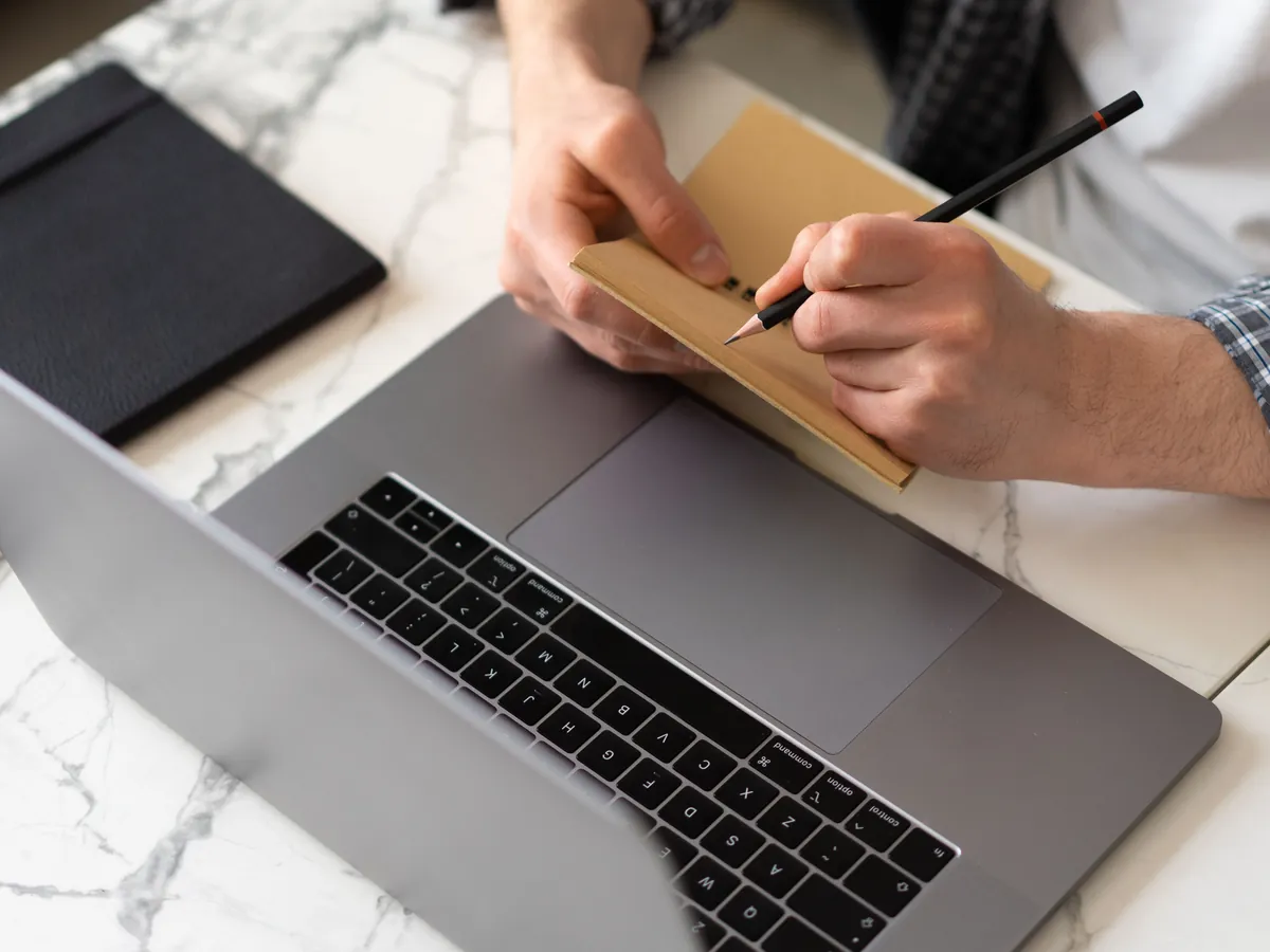 Professional learner taking structured notes while studying an online course on a laptop.